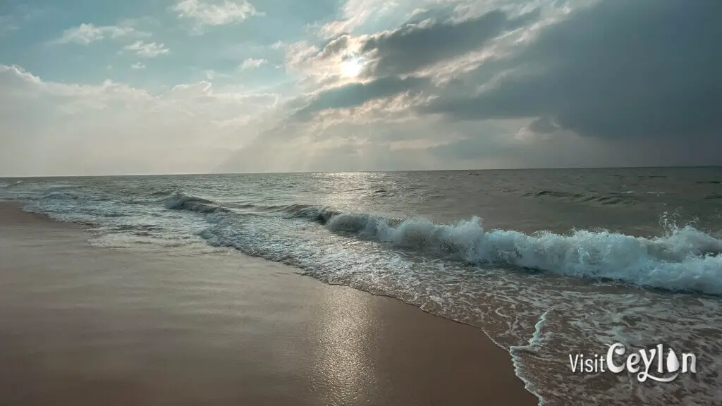 Beach view in the afternoon with bright sunlight, blue water, and a calm shoreline.